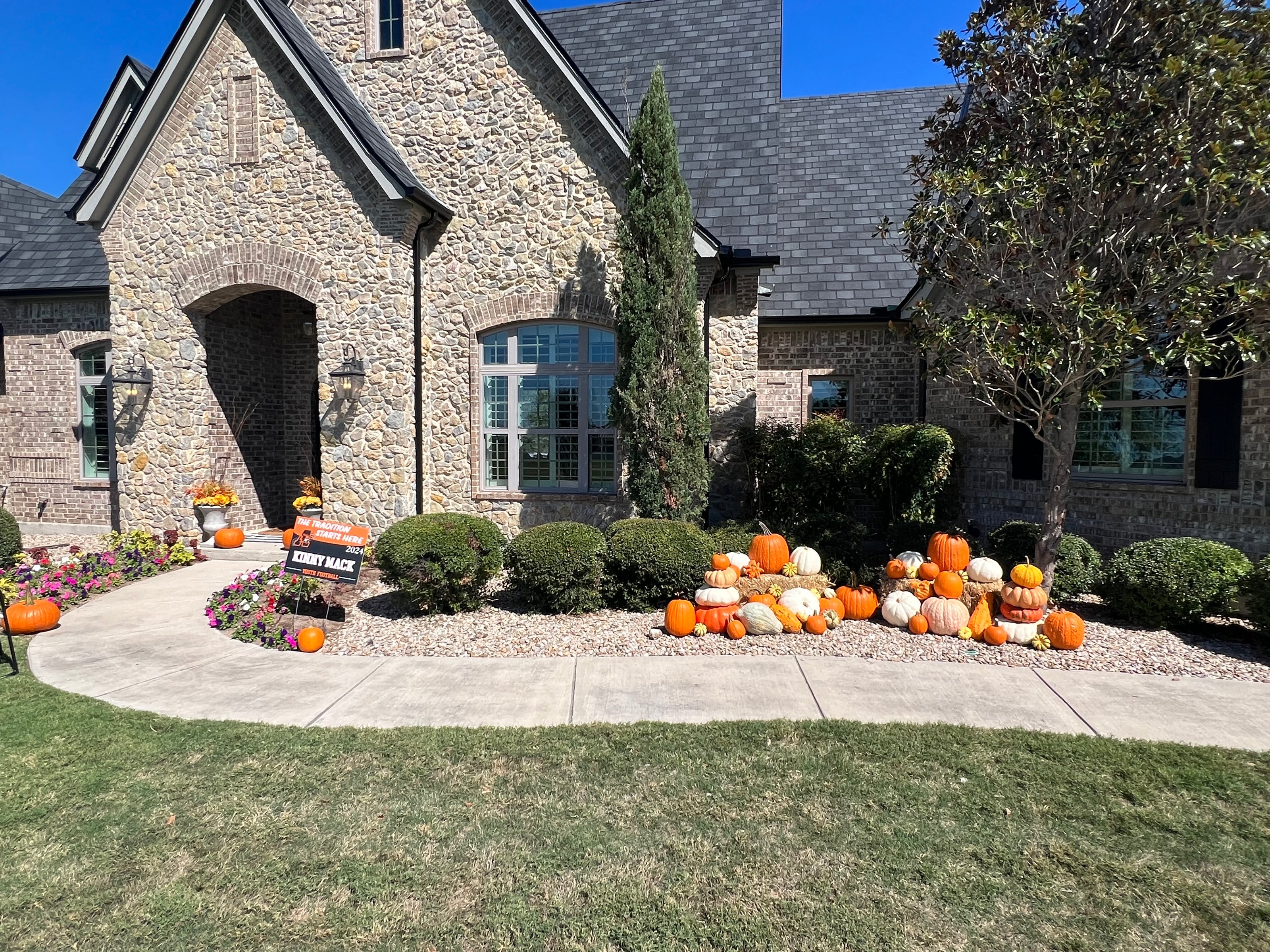 Decorative pumpkins in front of a stone house with a clear blue sky.